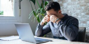 Homem sentindo cansaço nos olhos devido à fadiga ocular digital enquanto trabalha no notebook.
